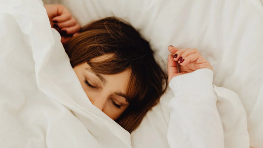 Femme couchée dans son lit. La couverture couvre la moitié de son visage. 